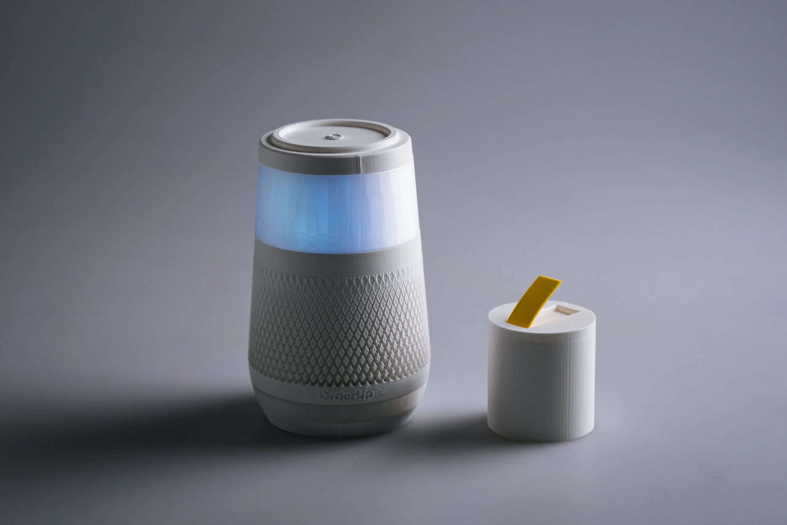 The OrderUP device with its glowing blue ring next to a small module with a yellow insert